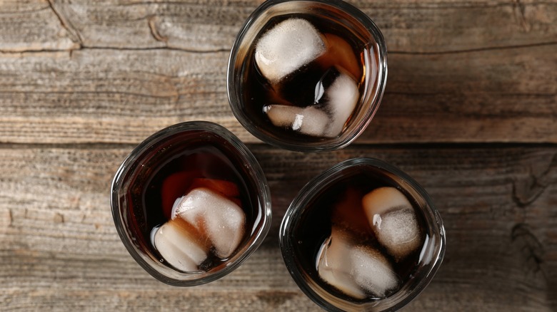 Three classes containing a dark beverage sit on a wooden table.