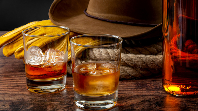 Two glasses of whiskey sit next to a cowboy hat