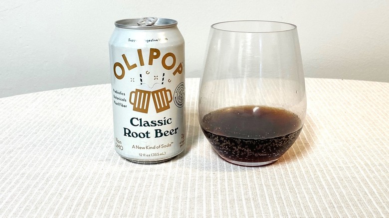 a can of Classic Root Beer Olipop sits on a table beside a sample in a glass