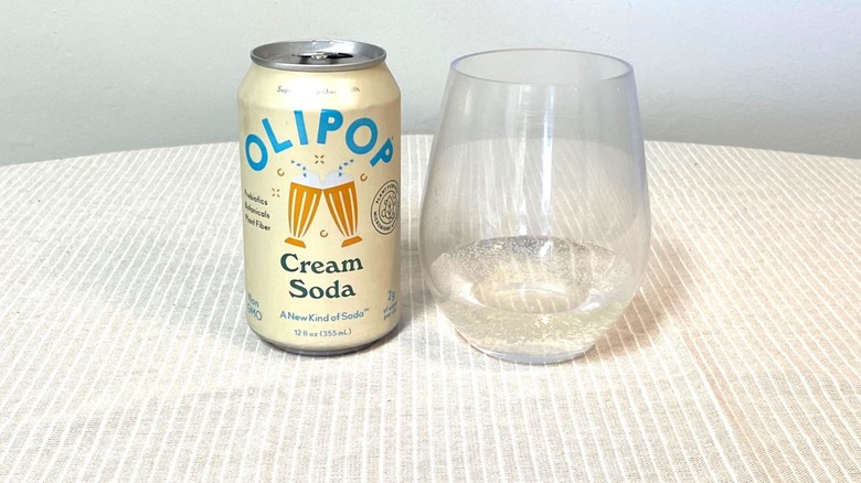 a glass of Olipop Cream Soda on a table beside its light yellow can