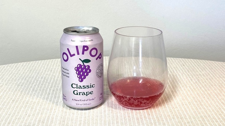 a can of Classic Grape Olipop on a table beside a glass containing a sample