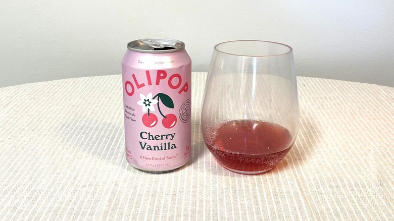 a pink can of Cherry Vanilla Olipop beside a glass of the soda on a table
