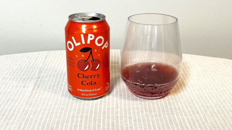 a red can of Cherry Cola Olipop beside a glass containing a sample