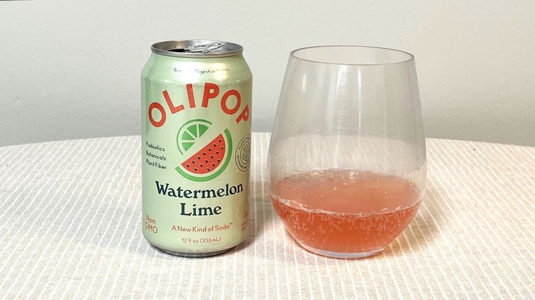 a glass of Olipop Watermelon Lime on a table beside its light green can