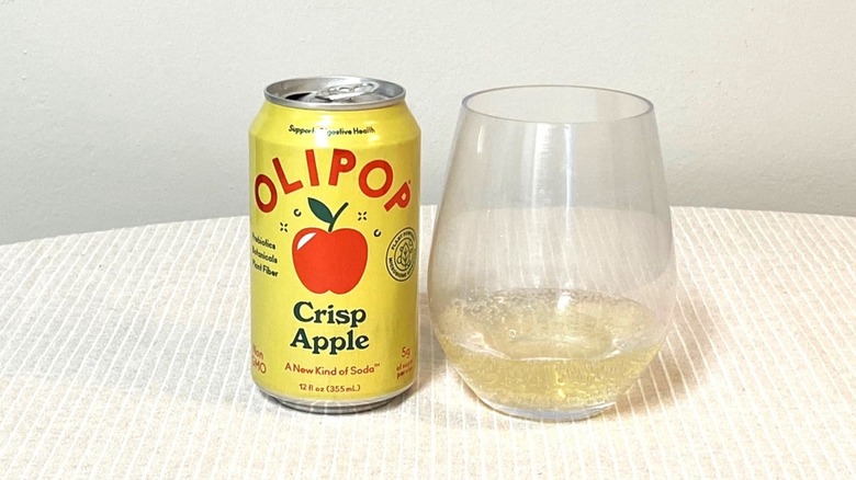 a glass of Olipop Crisp Apple on a table beside its bright yellow can