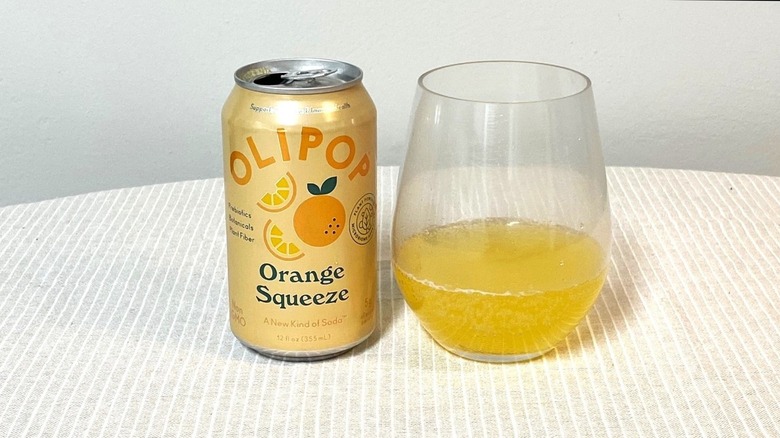 a can of Olipop Orange Squeeze sitting beside a glass containing a sample