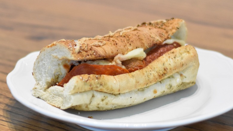 A meatball sub with pepperoni and cheese on herb cheese bread on a white plate