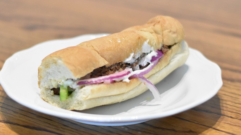 A Philly cheesesteak sandwich with red onion, green pepper, and mayo on a white plate