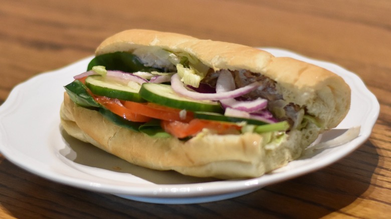 A chicken salad sandwich with cucumber, spinach, tomato, red onion, and lettuce on a white plate