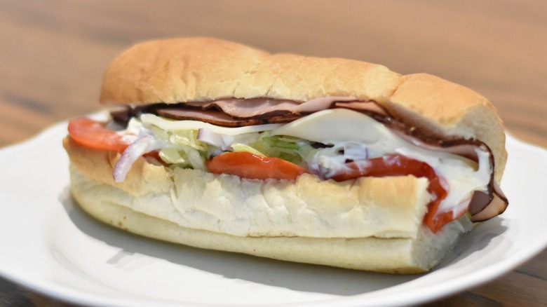 A ham sandwich with cheese, tomato, lettuce, red onion, and mayo on a white plate