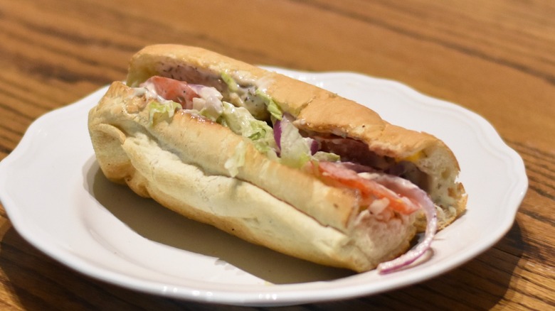 A rotisserie chicken sub sandwich with lettuce, tomato, red onion, and ranch dressing on a white plate