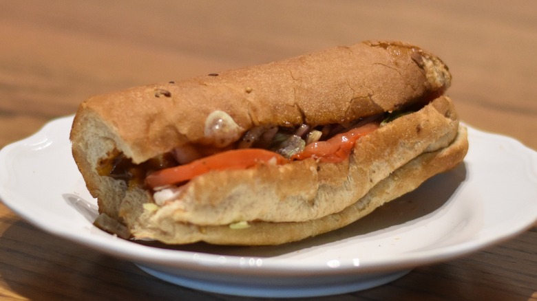 A rotisserie chicken sub sandwich with teriyaki sauce, tomato, and cheese on multigrain bread on a white plate