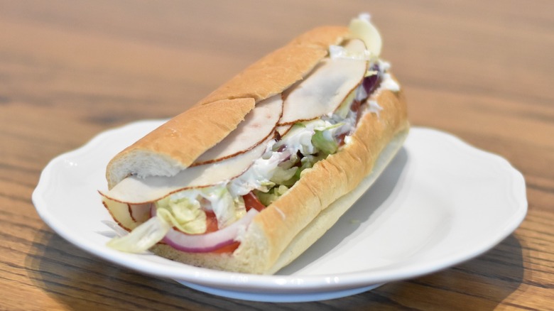 A turkey sandwich with mayo, cheese, tomatoes, and lettuce on a white plate