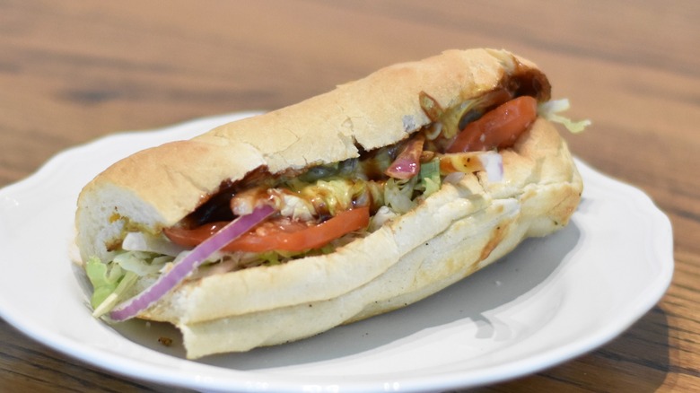 A chicken sub with honey mustard and barbecue topped with red onion, tomato, and lettuce on a white plate