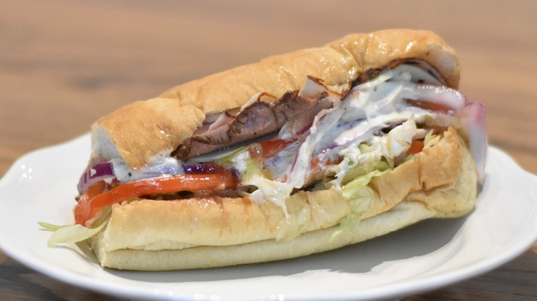 A Subway sandwich with turkey and roast beef slathered in mayo with tomato and lettuce on a white plate