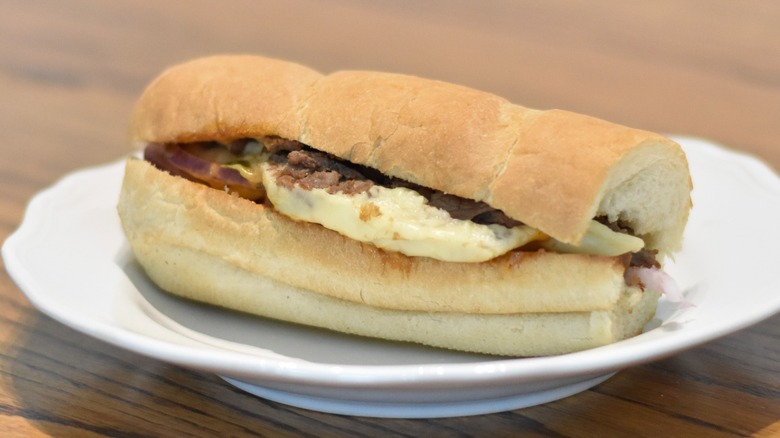 A beef sub sandwich with cheese on white bread on a white plate