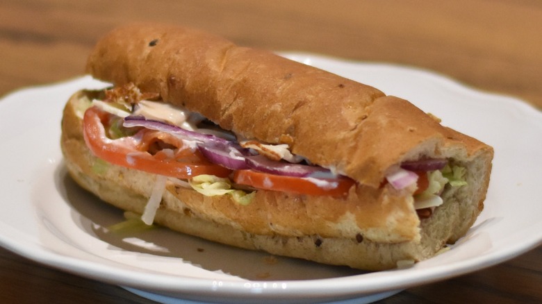 A club sub sandwich with tomato, red onion, lettuce, and cold cuts on multigrain bread on a white plate