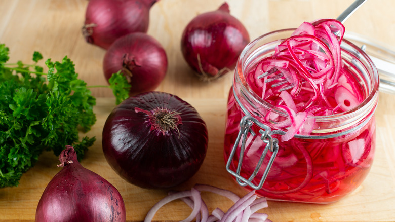 pickled red onions in a jar next to whole red onions