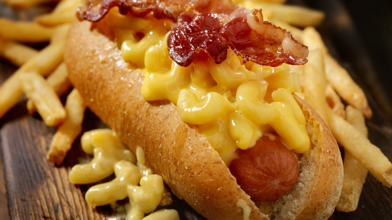 A hot dog topped with mac and cheese and bacon