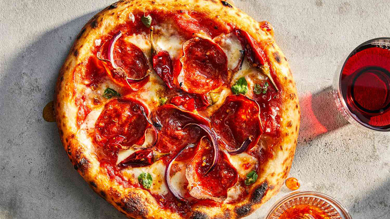 A pizza with Calabrian chiles, soppressata, and onions on a table