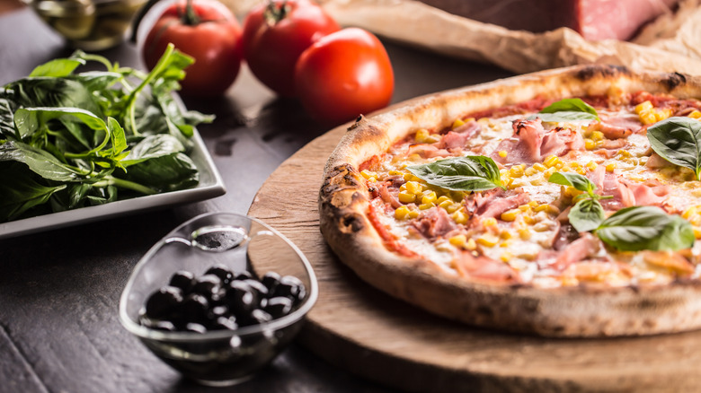 A pizza with corn and prosciutto on a wooden board