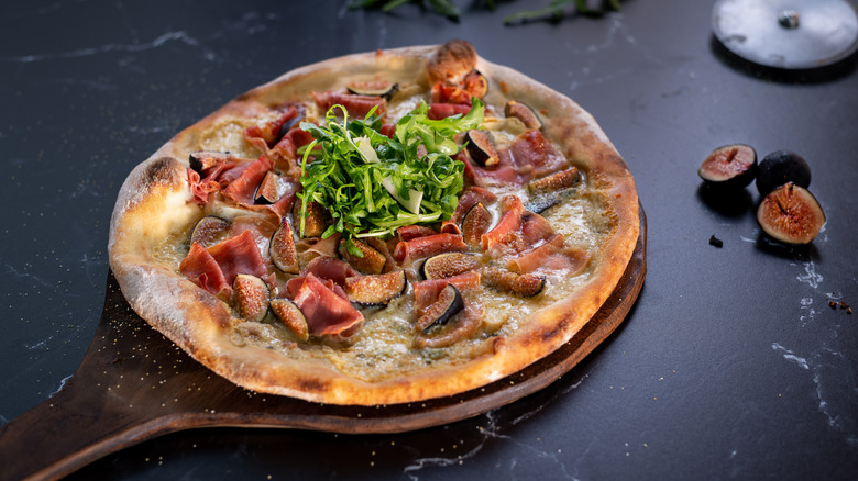 A pizza with figs, prosciutto, and arugula on a wooden paddle