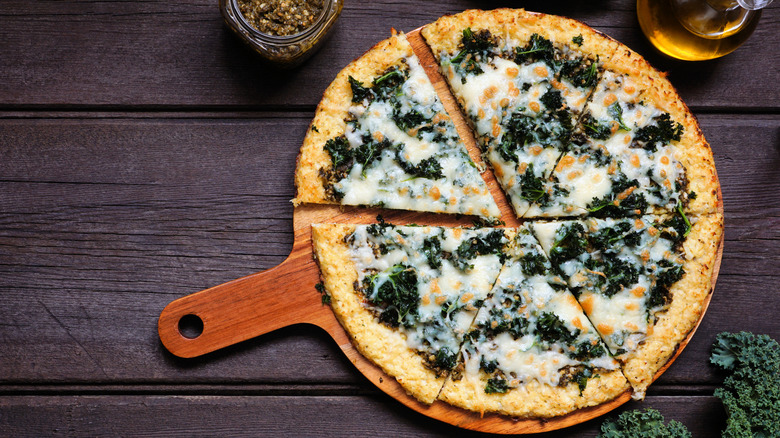 A cauliflower crust pizza with fried kale and cheese on a pizza paddle