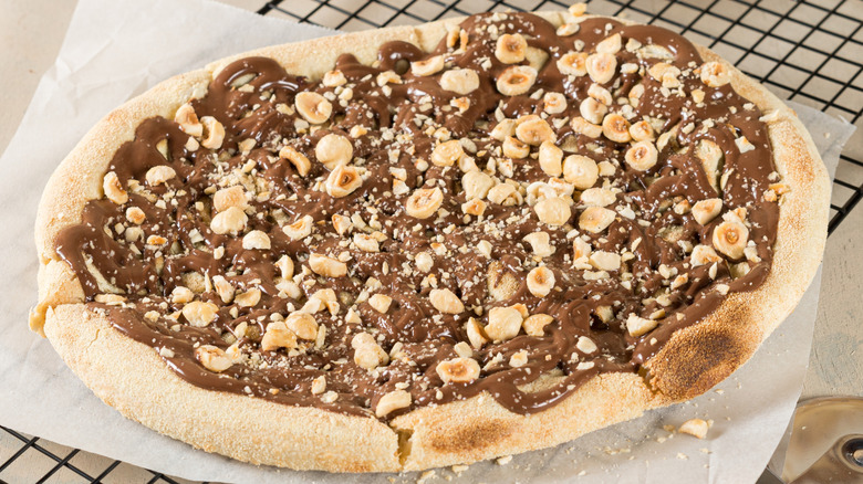 A dessert pizza with Nutella and hazelnuts on a cooling rack