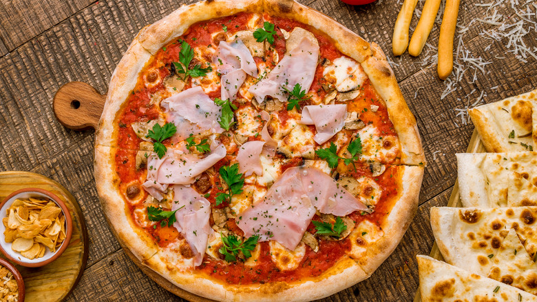 A pizza with mortadella and red sauce with sides on wooden board