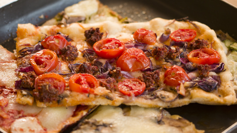 A slice of homemade pizza with nduja sausage and cherry tomatoes