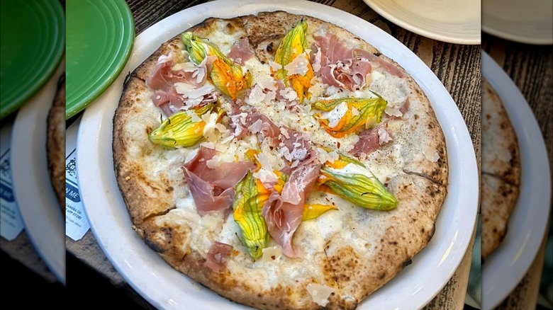 A pizza with squash blossoms and prosciutto on a plate