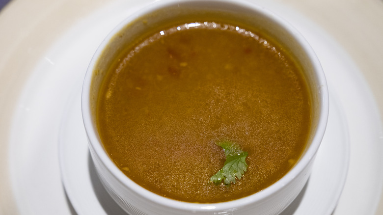 Beef broth in bowl with herbs floating on top