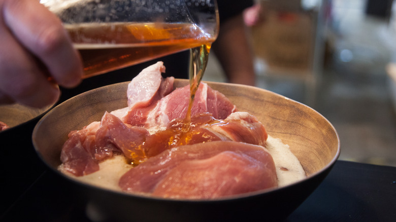 Person pouring beer over meat while cooking