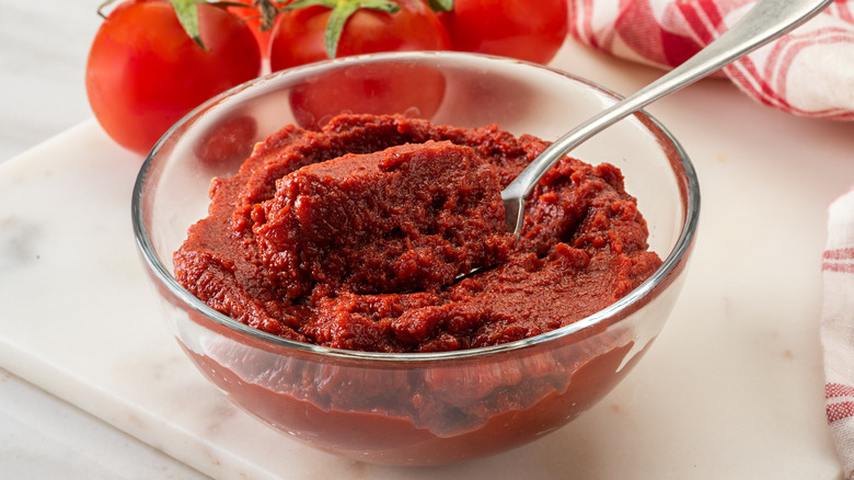 Glass bowl of tomato paste with spoon on white countertop