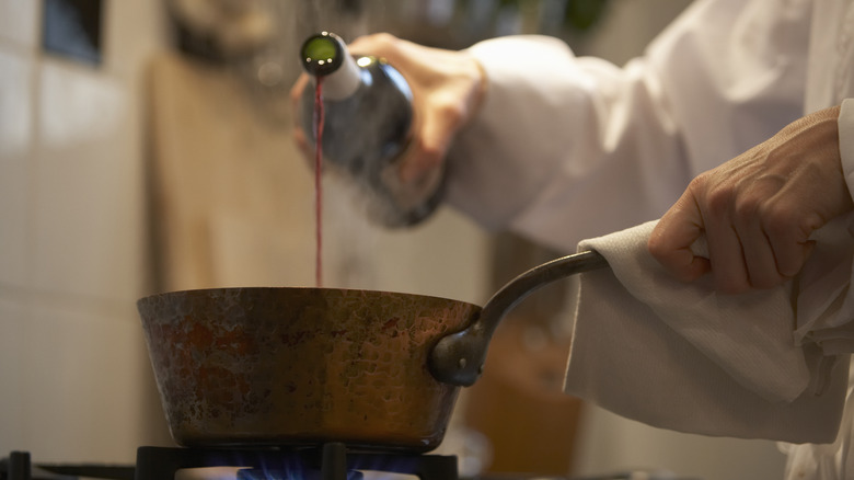 Woman adding red wine to a pot on the stove