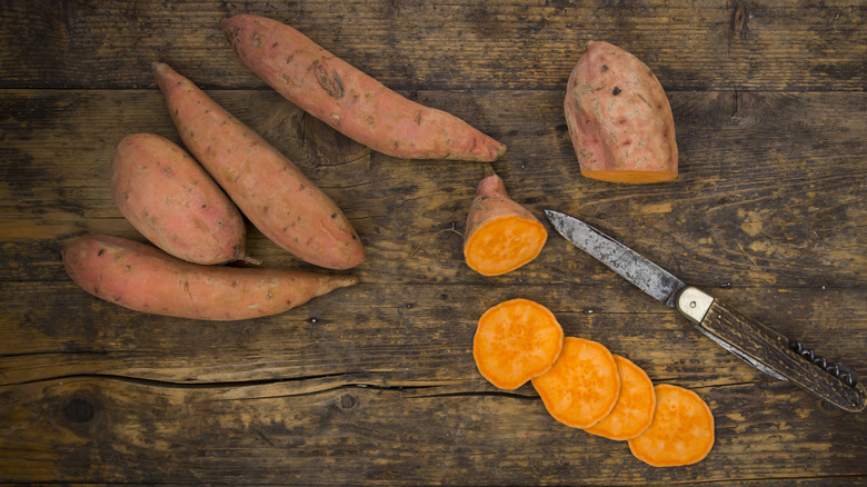 Sliced and whole sweet potatoes on a cutting board with a knife