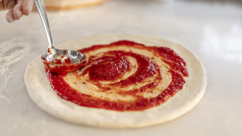 Person spreading pizza sauce on pizza with the back of a spoon