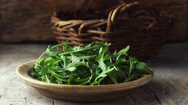 Fresh arugula on a plate in front of a woven basket