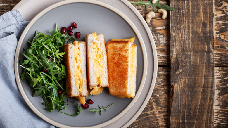 Halved scrambled egg sandwiches on a plate with arugula and pomegranate seeds