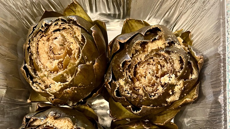 Two stuffed artichokes in a disposable foil pan