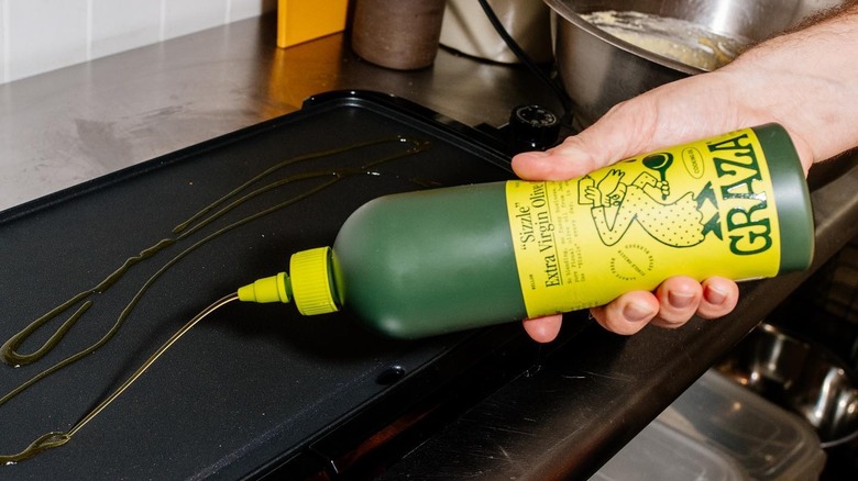 Hand squeezing Graza oil bottle onto griddle