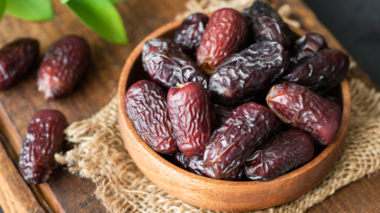 dried dates in wooden bowl with plant in background