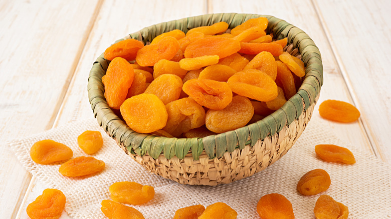 dried apricots  in basket on beige woven fabric and wooden table