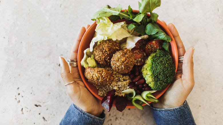 hands surrounding bowl of falafel and greens