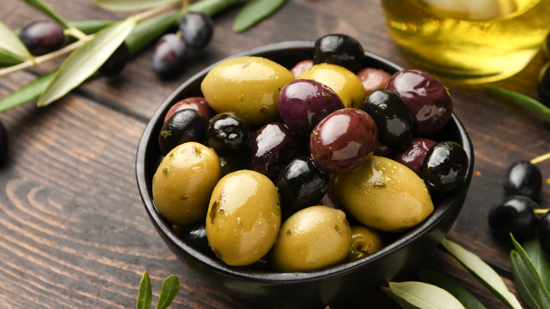 mixed olives in bowl on wooden table with olive leaves