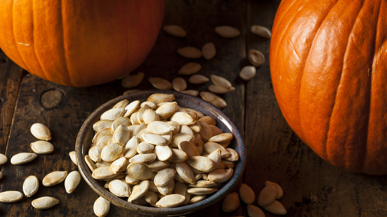 Roasted pumpkin seeds in a bowl with whole pumpkins in the background