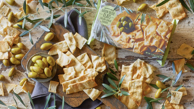 Green Olive Flats Italian Lingue Crackers package with crackers scattered about and a dish of olives on a cutting board
