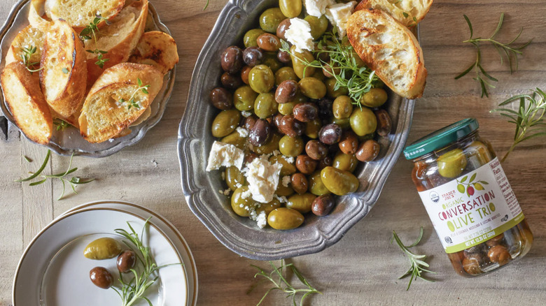 Organic Conversation Olive Trio laying next to bowls of olives and grilled bread