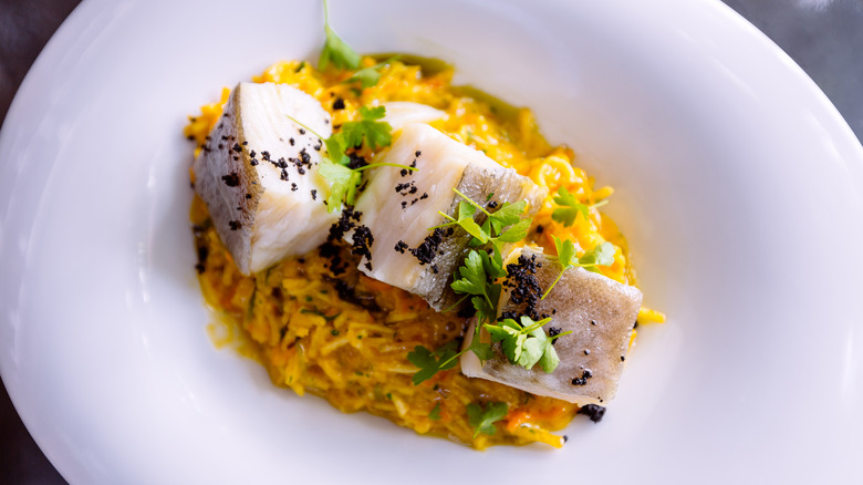 Pieces of bacalhau salted cod sit in a white dish.