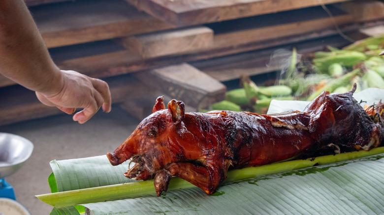 A person reaches for a piece of lechon spit roasted pig in the Philippines.